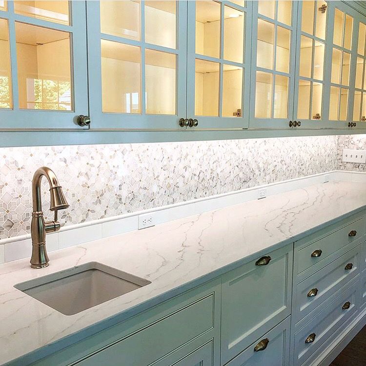Light blue kitchen with glass-front cabinets, white countertops, and a silver faucet.