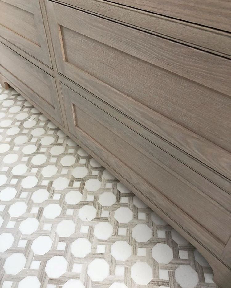 Wooden cabinet with recessed panels above geometric patterned floor tiles.