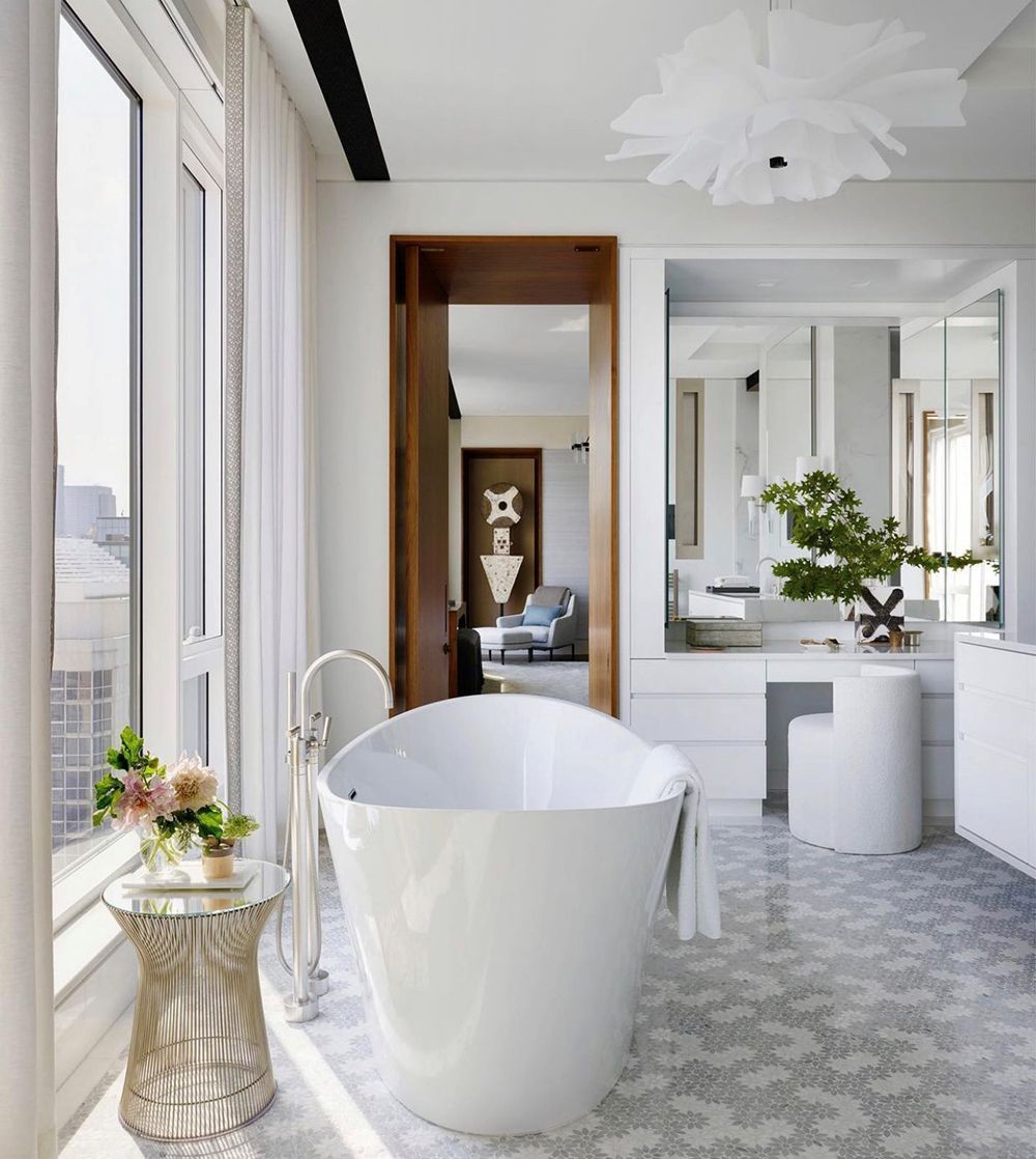 Bright white bathroom with a freestanding tub, large window, and patterned tile floor.