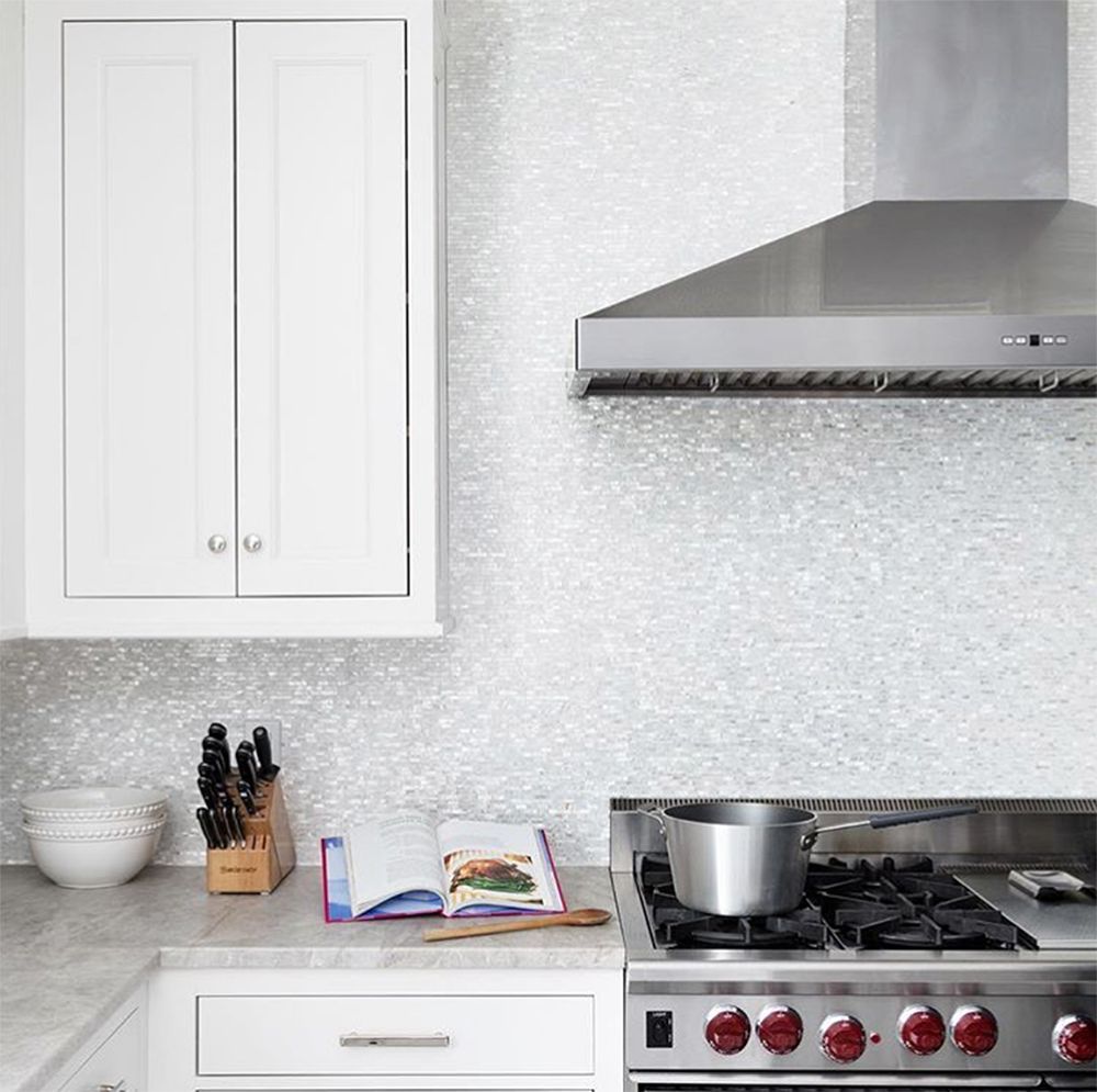 White kitchen with stainless steel range hood, stove, cabinets, and a pot on the burner.