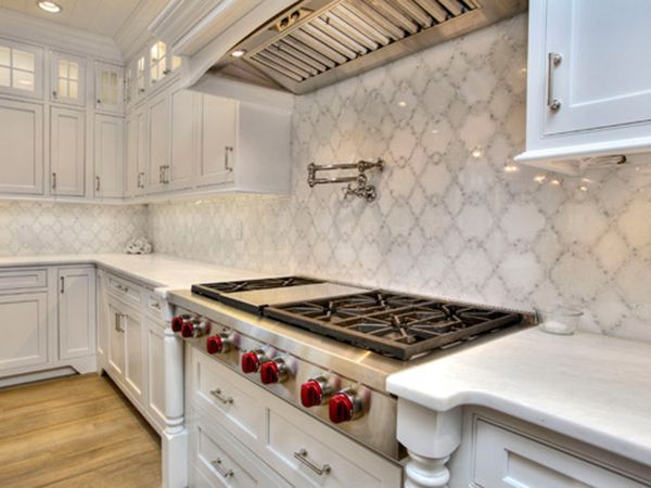 White kitchen with marble backsplash, stainless steel stove with red knobs, and cabinets.