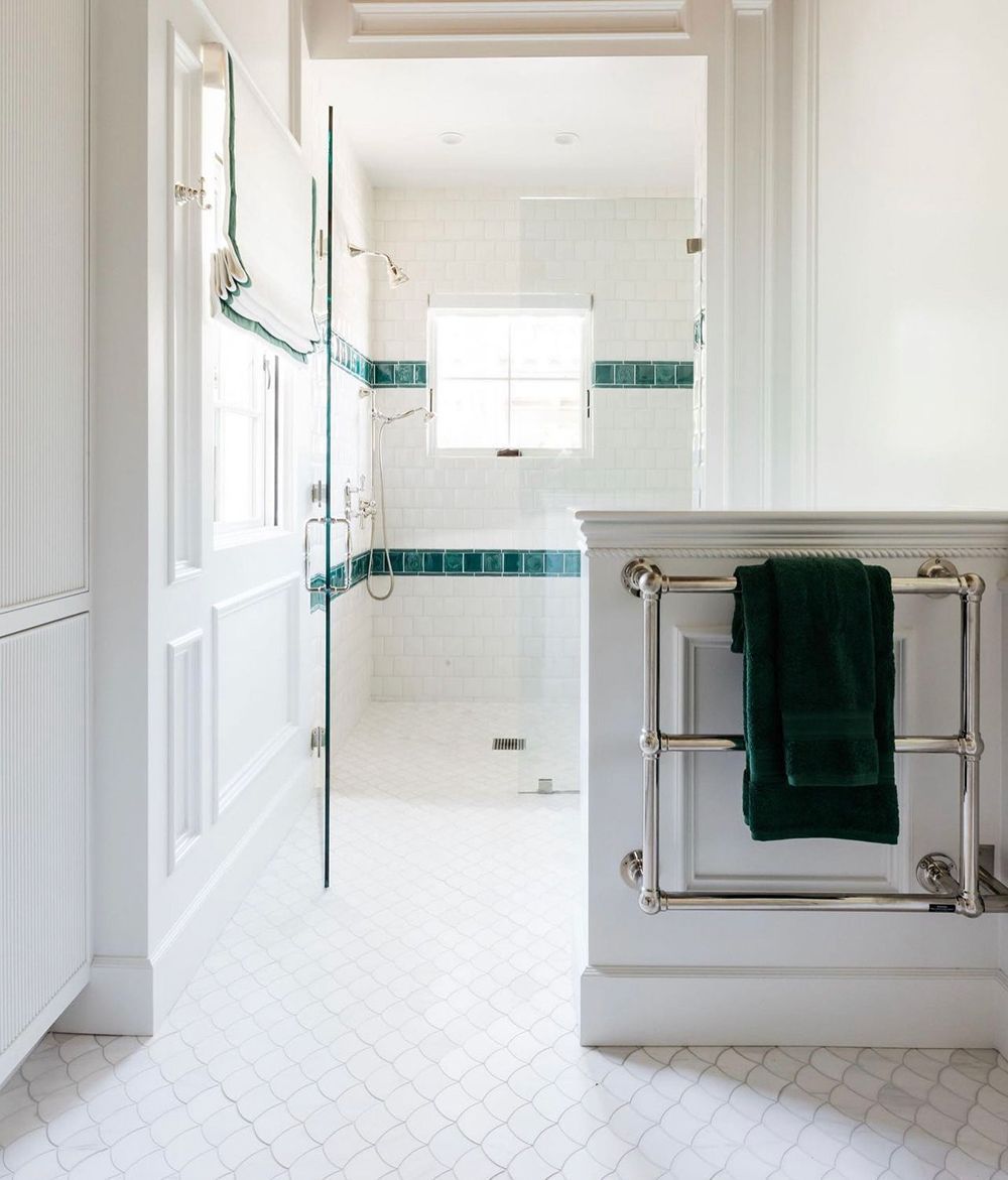 White bathroom with teal accent tile, a heated towel rack, and a glass-enclosed shower.