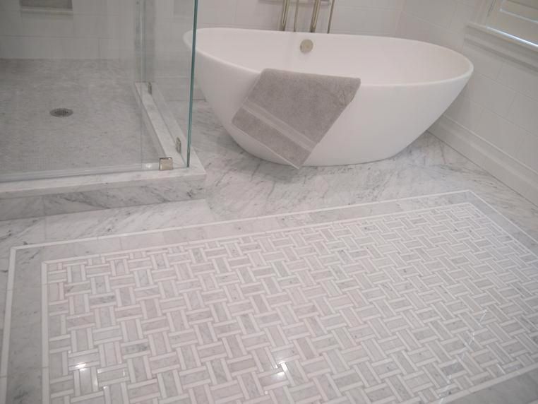 Bathroom with white oval tub and shower, marble floor with patterned tile detail.