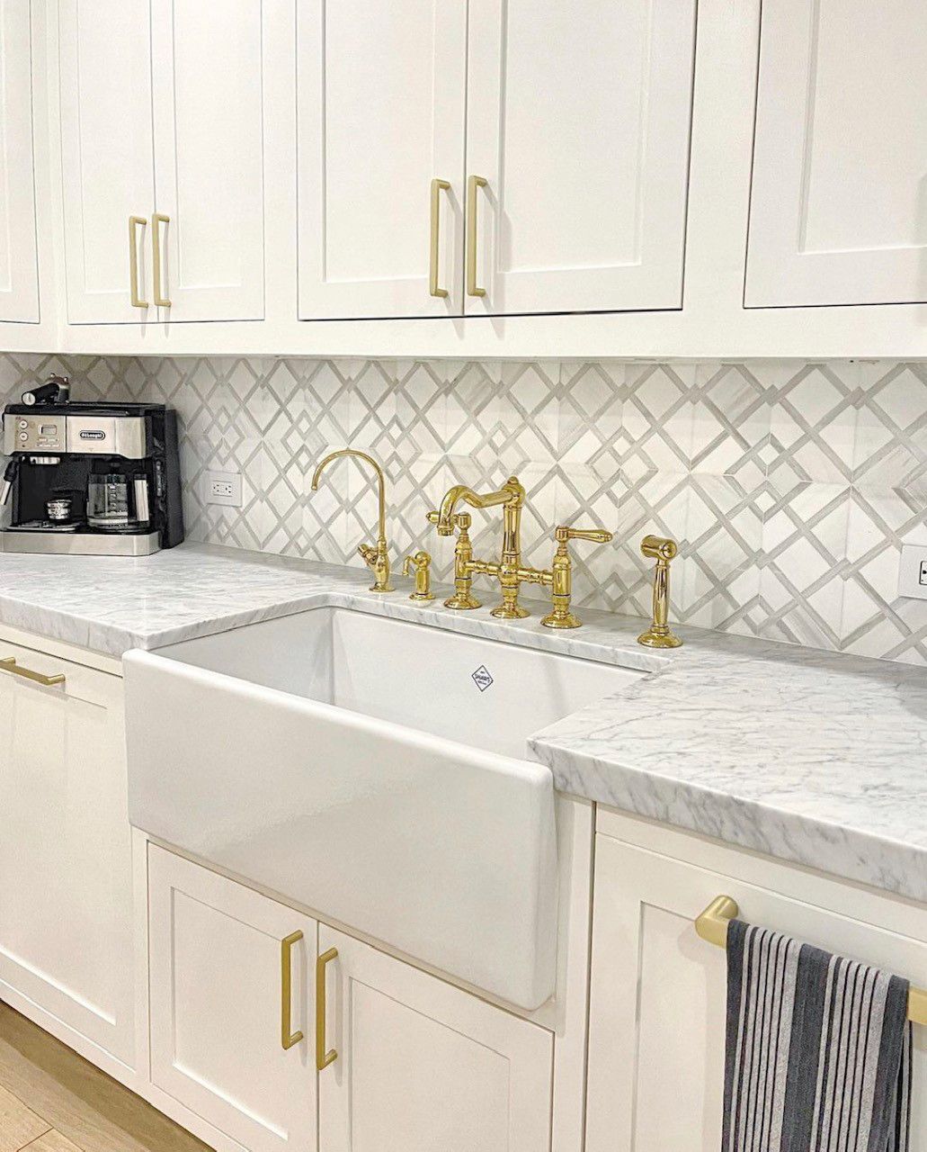 White kitchen with marble countertops, farmhouse sink, gold faucet, and cabinets.
