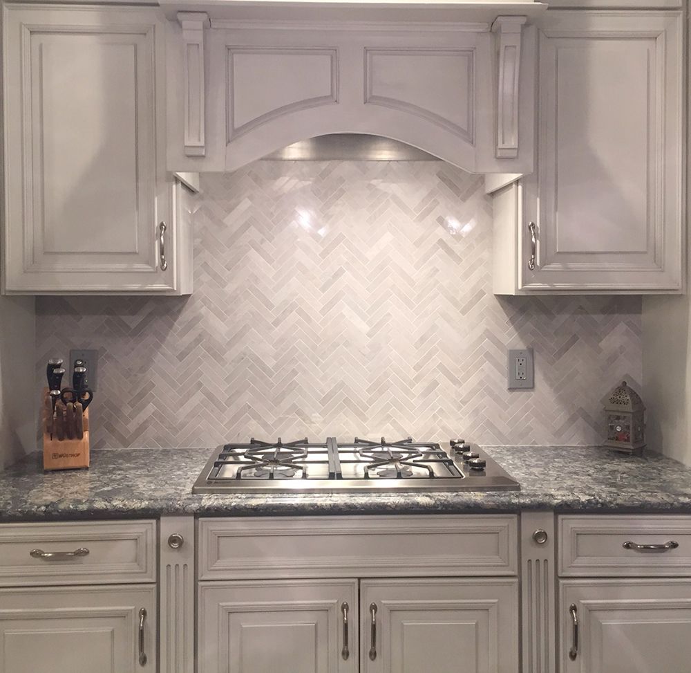 Kitchen with light grey cabinets, grey and white herringbone backsplash, and stainless steel range.