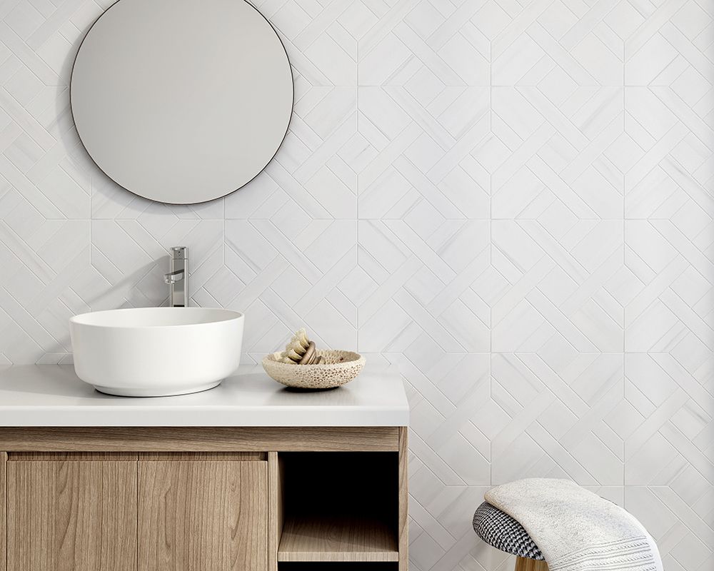Bathroom with a white sink, round mirror, and wooden vanity against white patterned tile.