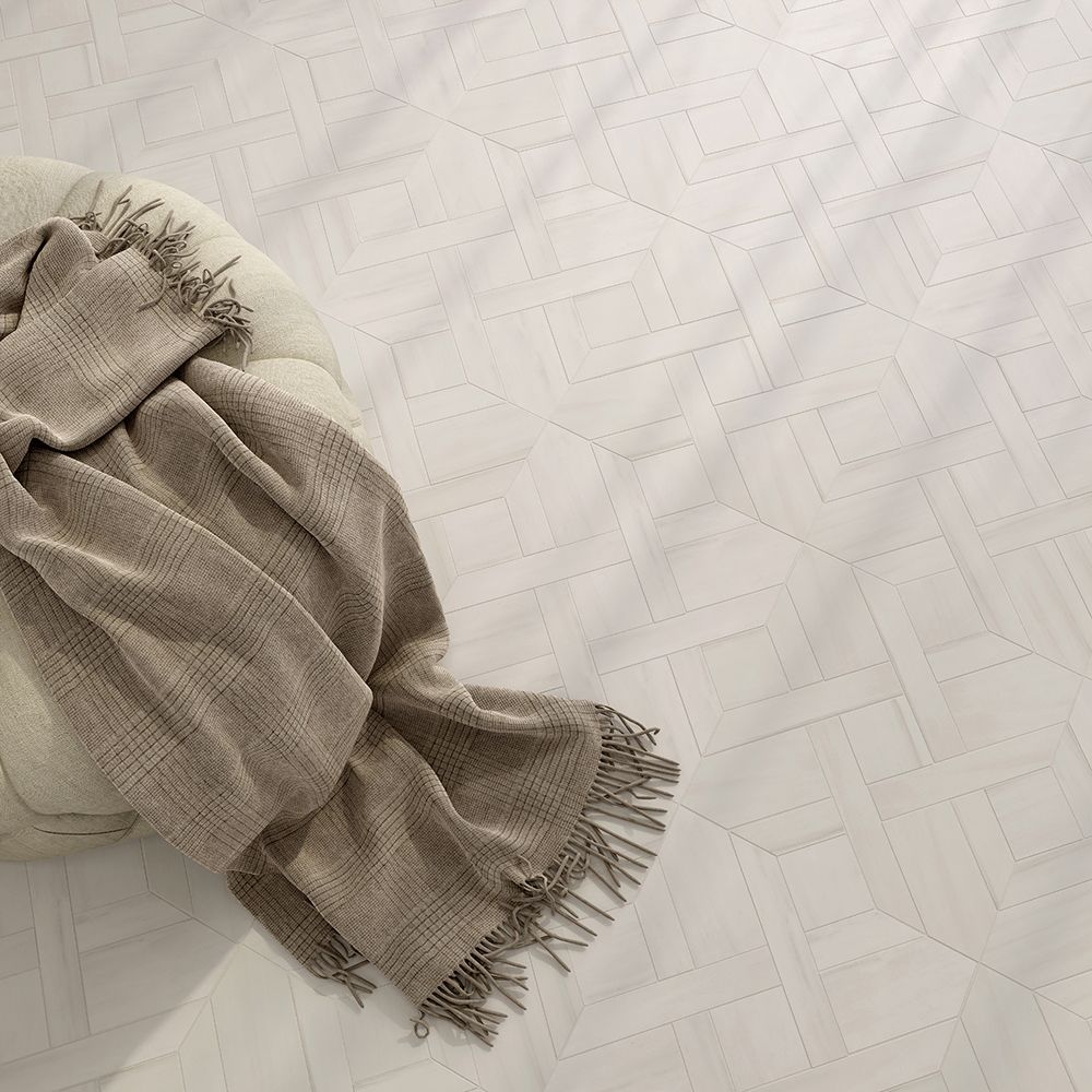 Beige throw blanket draped over a round cushion, on a white patterned surface.