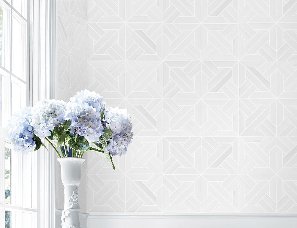 Hydrangeas in white vase by a window and white geometric patterned wallpaper.