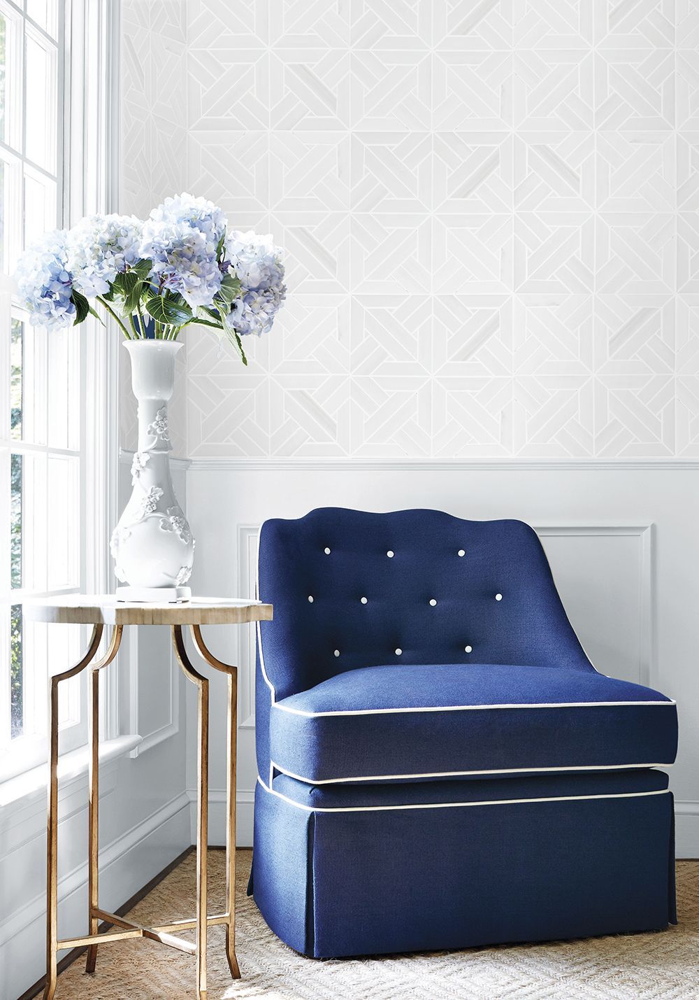 Blue upholstered chair beside a small table with vase of blue flowers, set by a window.