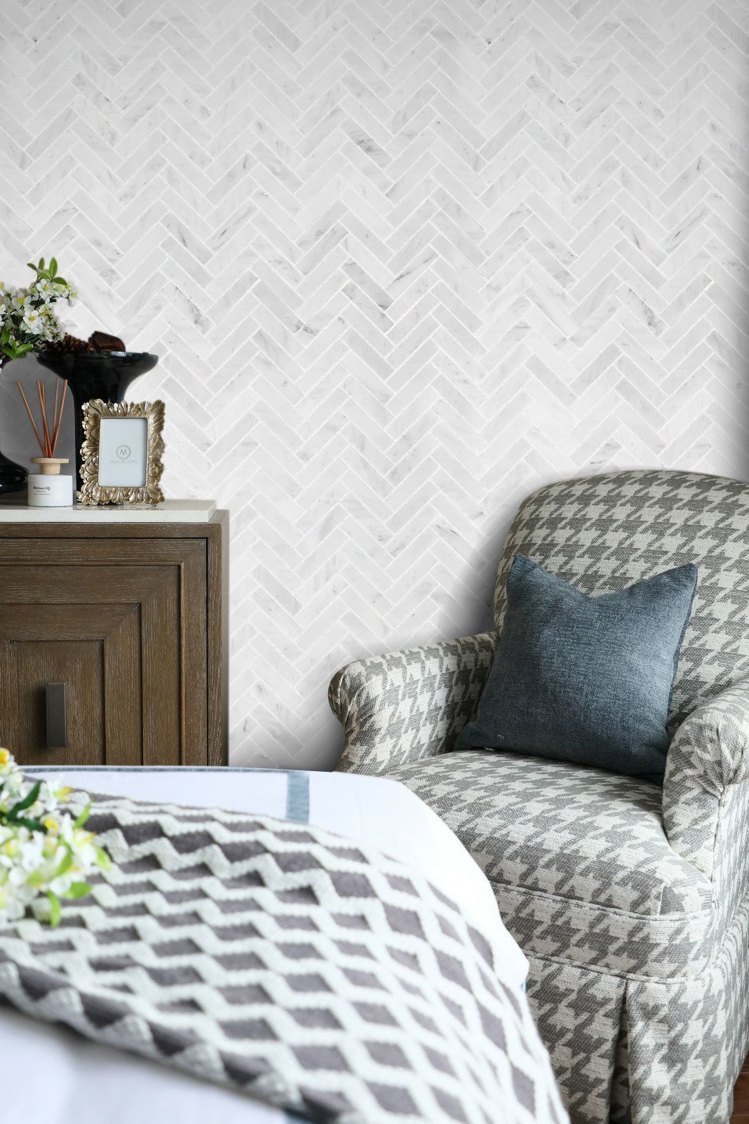 Armchair with houndstooth pattern, next to a cabinet with decor. White herringbone wallpaper in the background.