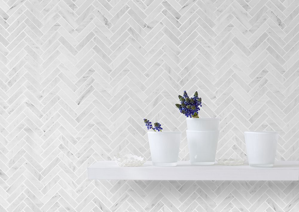 White herringbone tile backsplash with a white shelf holding three white vases and purple flowers.