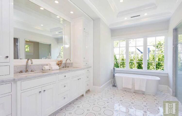 White bathroom with marble countertops, large mirror, and soaking tub by a window.