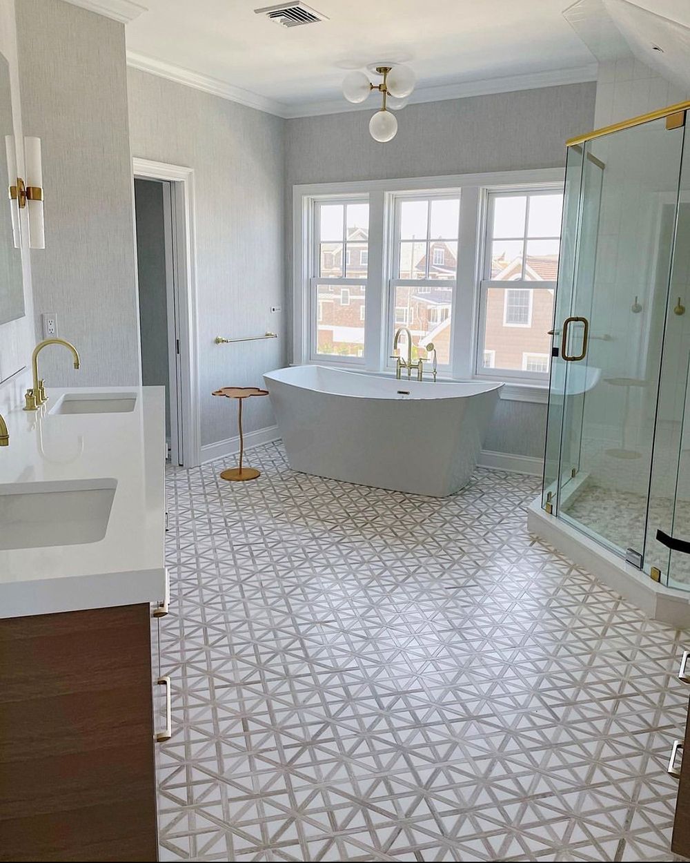 Spacious bathroom with patterned floor, freestanding tub, glass shower, and gold fixtures.