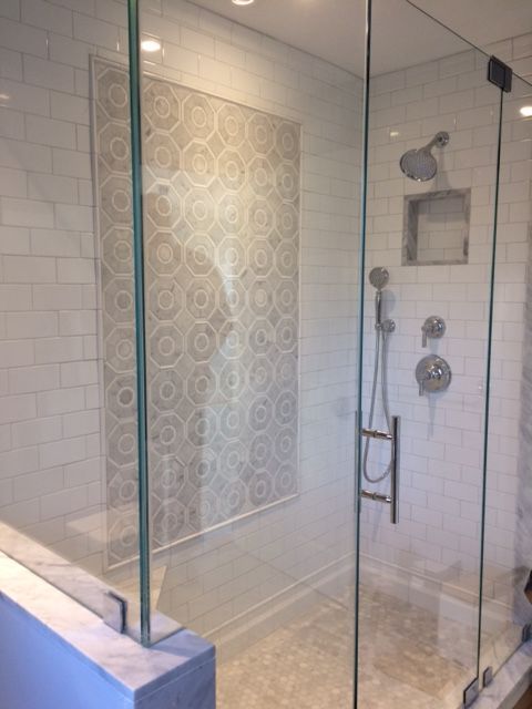 Modern shower with glass doors, white subway tile walls, patterned accent wall, and silver fixtures.