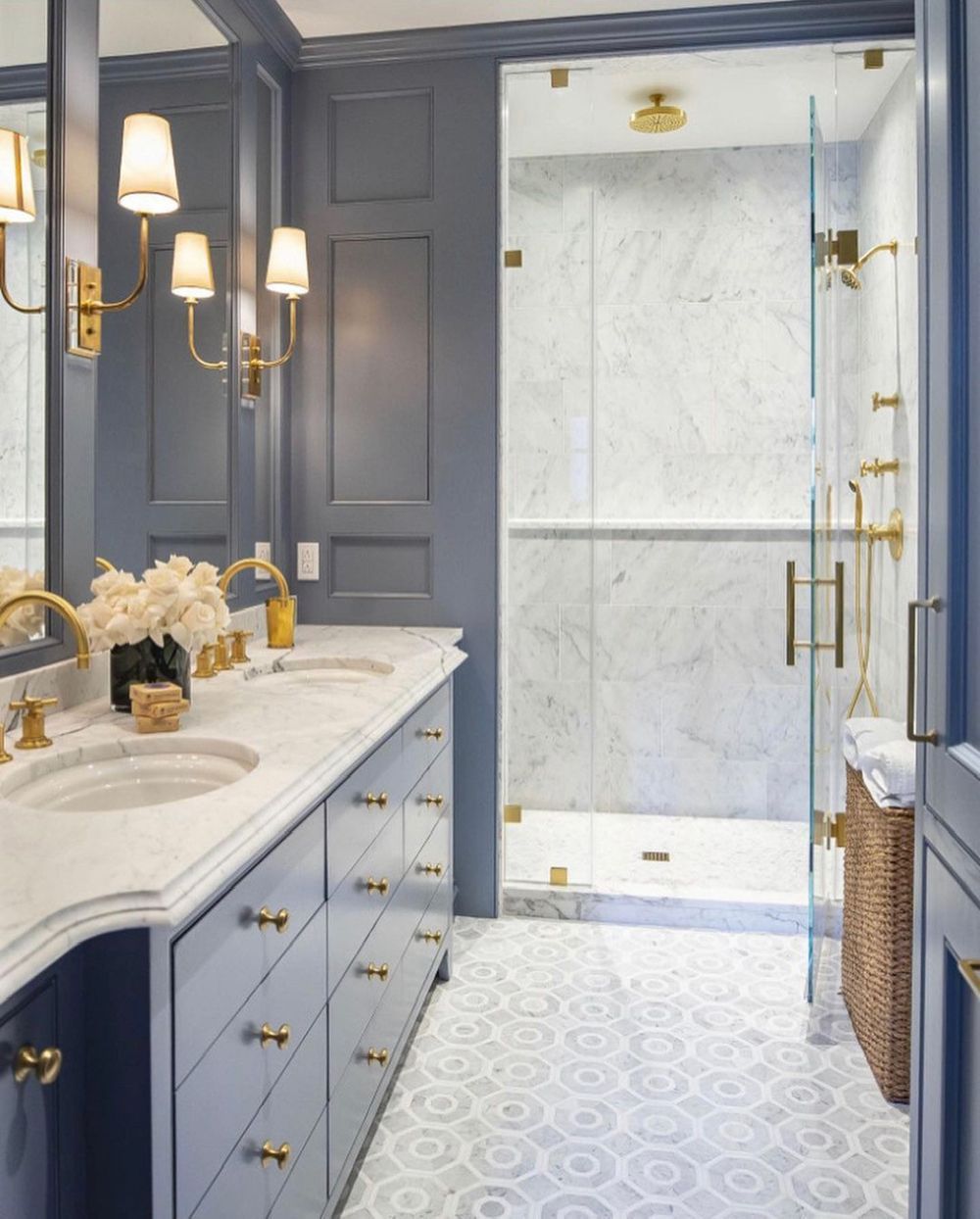 Blue bathroom with marble countertops, gold fixtures, and a glass shower.