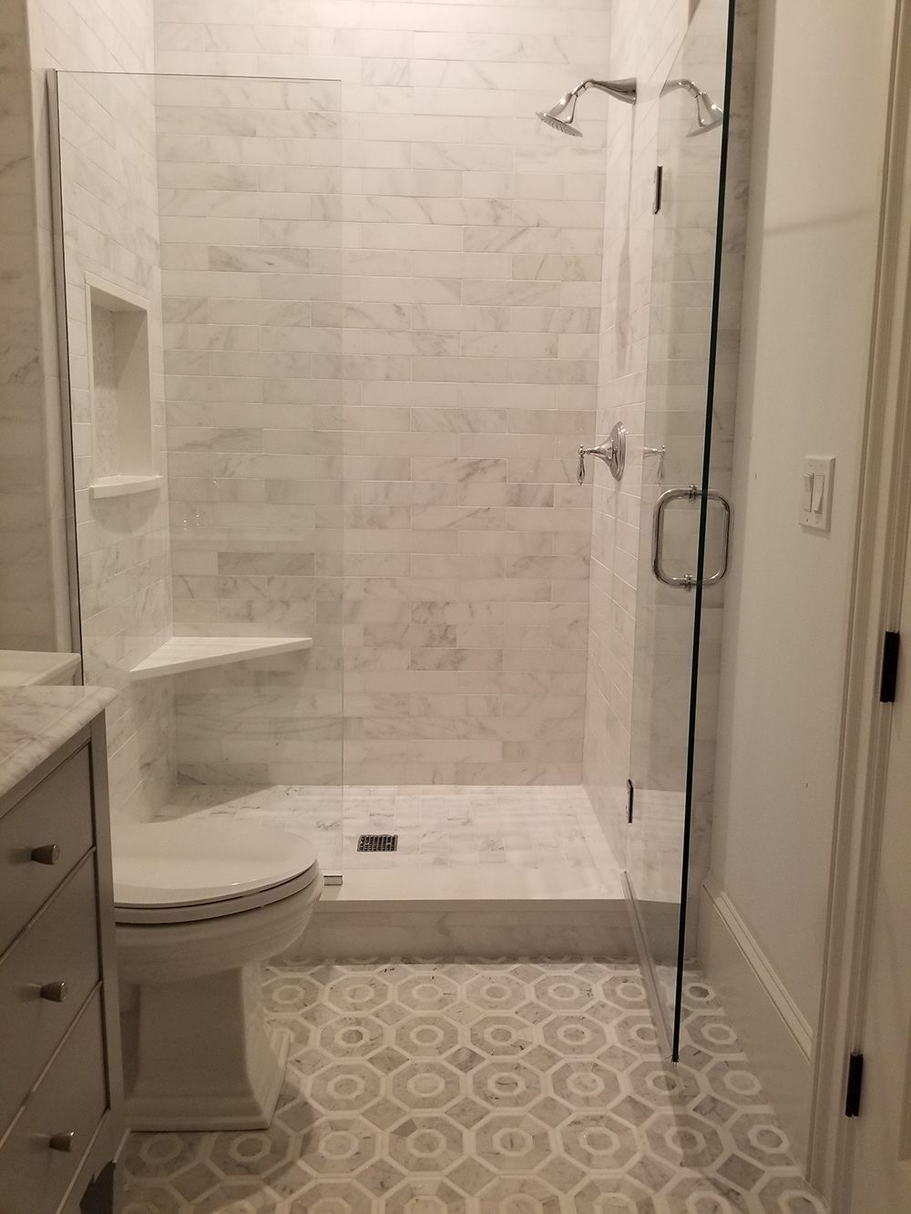 Bathroom with white marble shower, clear glass doors, and patterned floor tile.