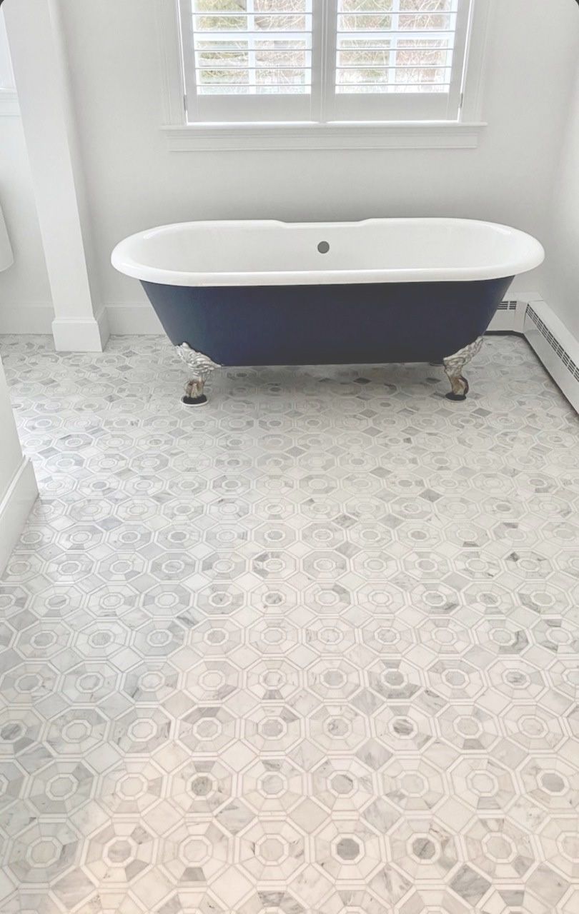 Bathroom with a blue clawfoot tub, patterned gray and white tiled floor, and window with blinds.