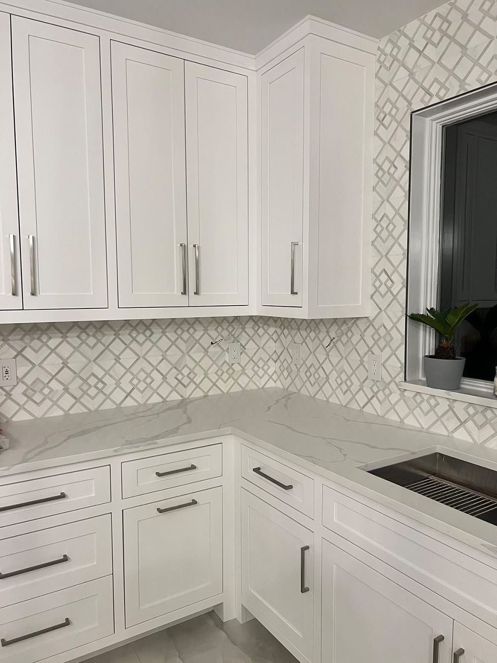 White kitchen cabinets and countertops with patterned backsplash.