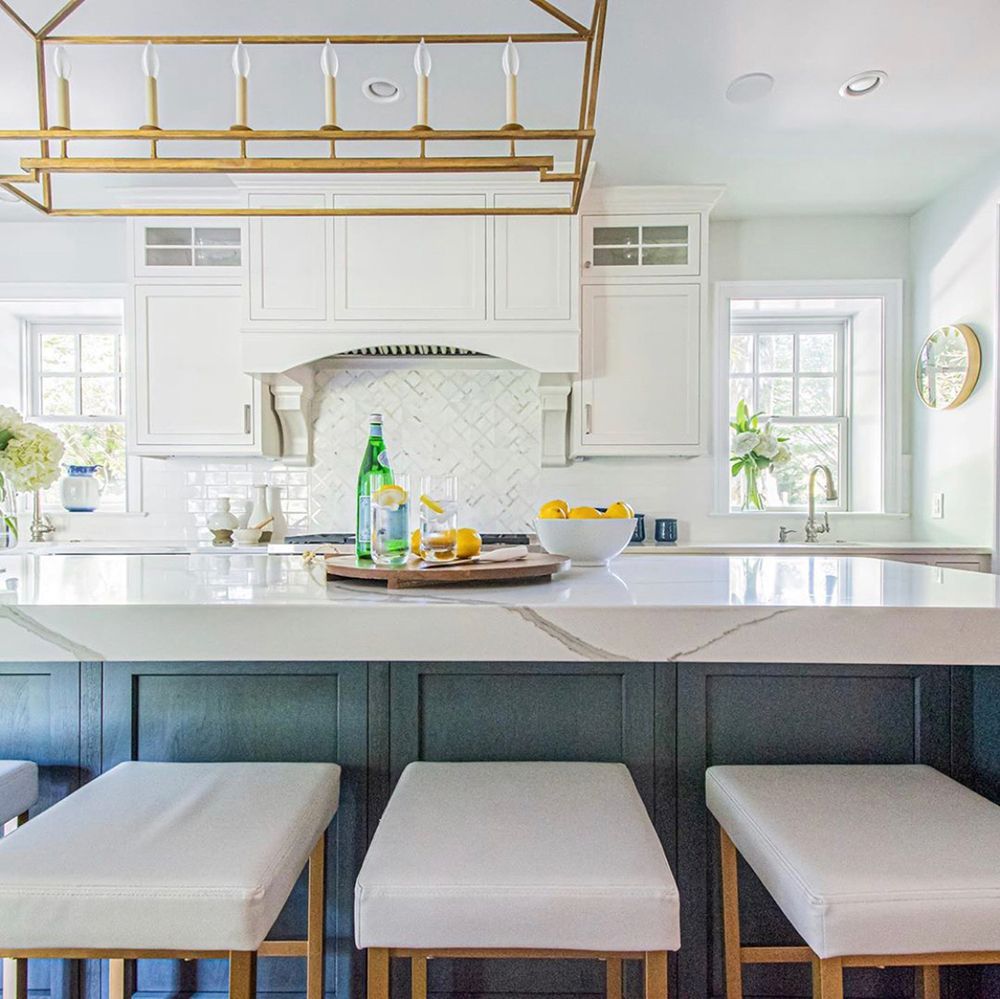 Stylish kitchen with white cabinets, blue island, marble countertop, and gold accents.