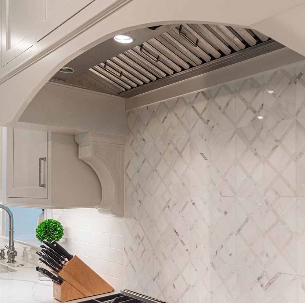 Kitchen range hood with marble backsplash, cabinets, and a decorative bracket.