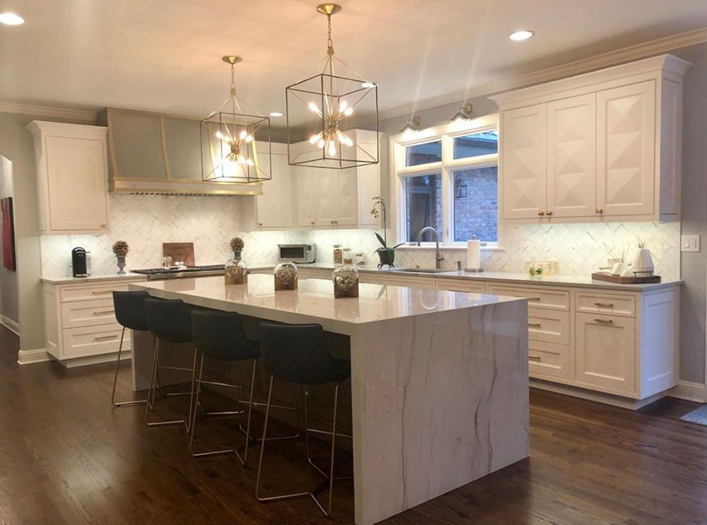 Modern kitchen with white cabinets, island, stools, and gold light fixtures.