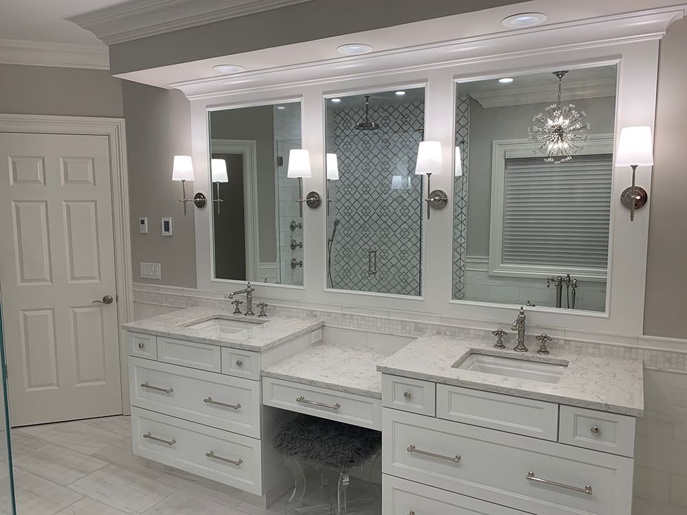 White bathroom with double vanity, three mirrors, and a glass-enclosed shower.