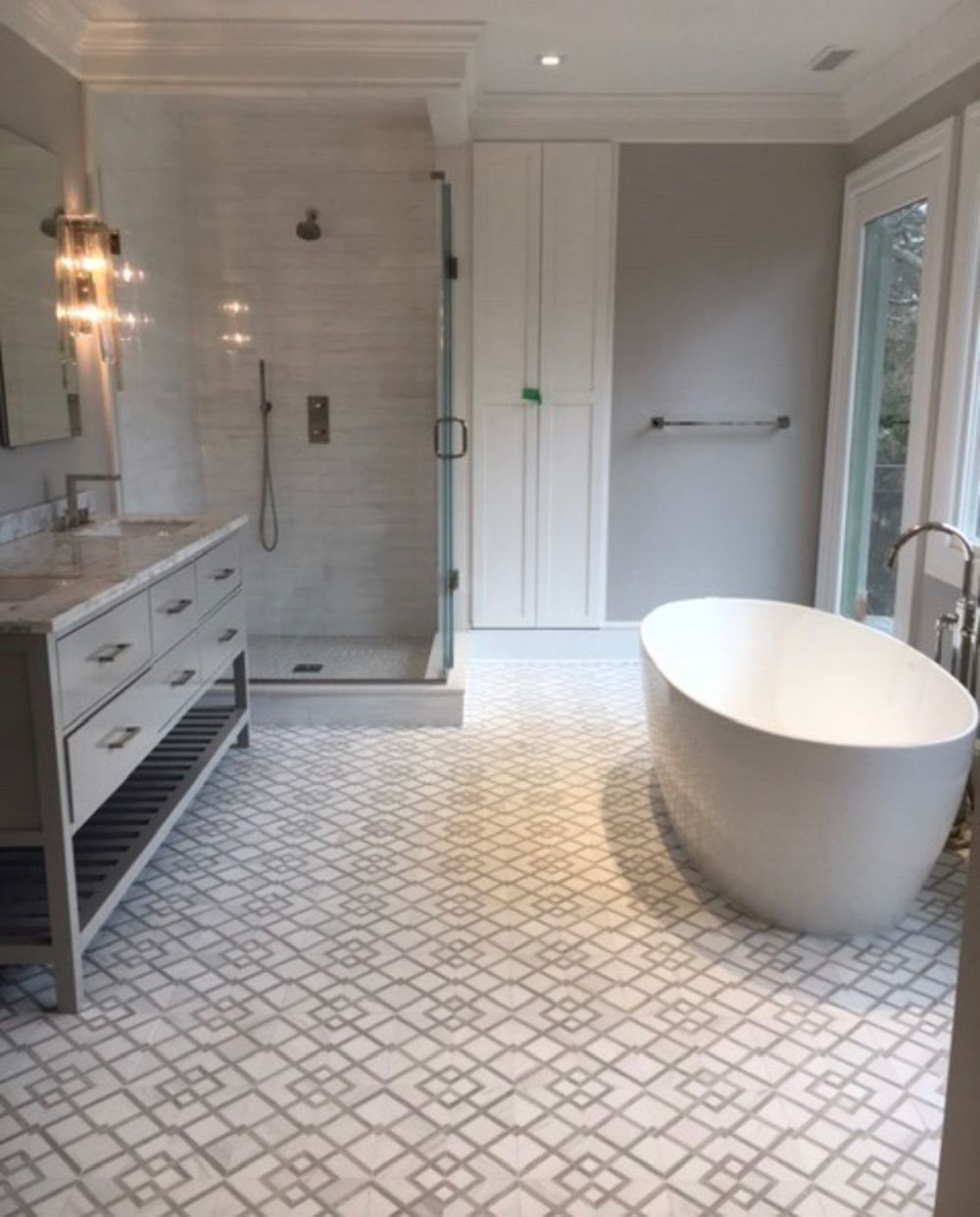 Bathroom with white and gray patterned tile, glass shower, vanity, and freestanding oval tub.