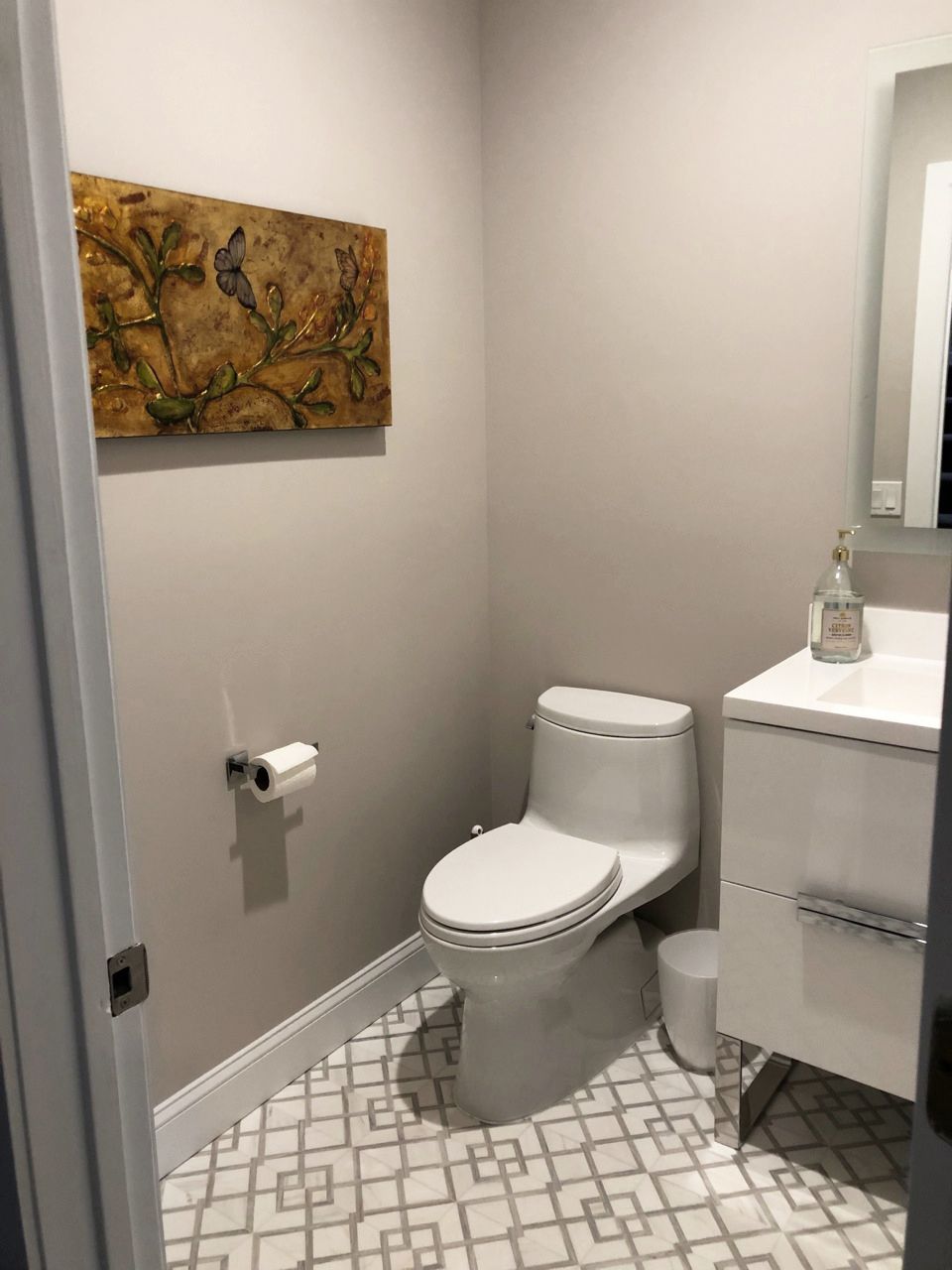 Powder room with a white toilet, sink, and gray patterned floor. Artwork hangs on the wall.