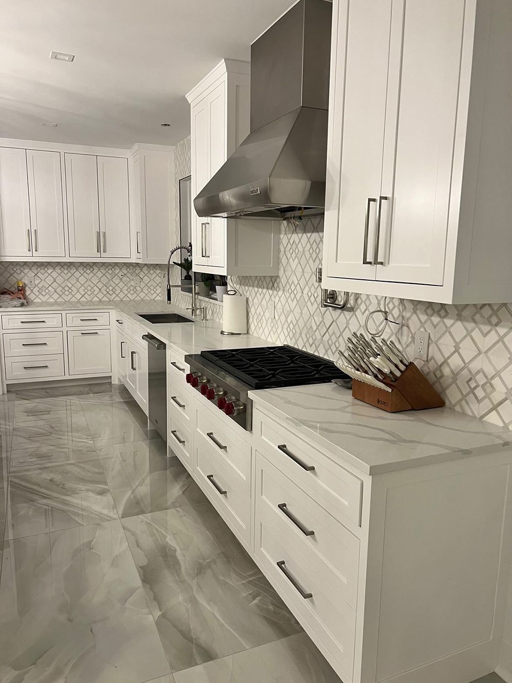 White modern kitchen with a large range and vent hood, white cabinets, and patterned backsplash.
