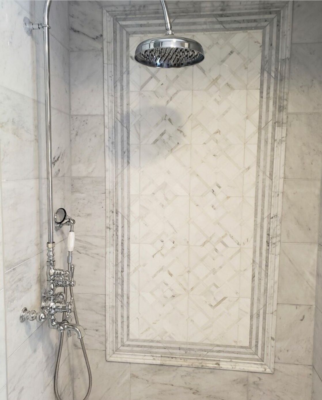 Shower with marble walls and a patterned tile accent. Chrome showerhead and fixtures.