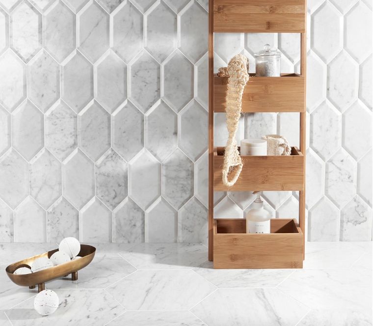 White marble bathroom with geometric tile, bamboo shelf, and bath products.