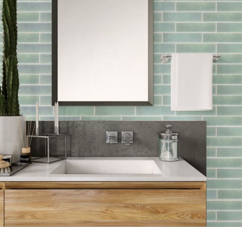 Bathroom with wooden vanity, white countertop, mint green subway tile, and a square mirror.