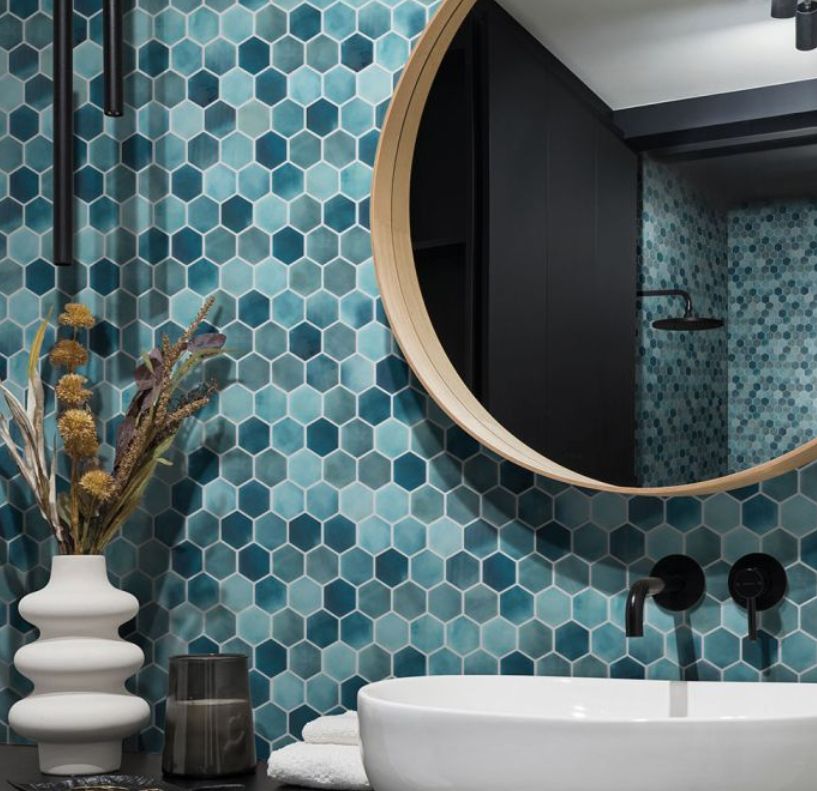 Bathroom with turquoise hexagon tile, round mirror, white sink, and black faucet.