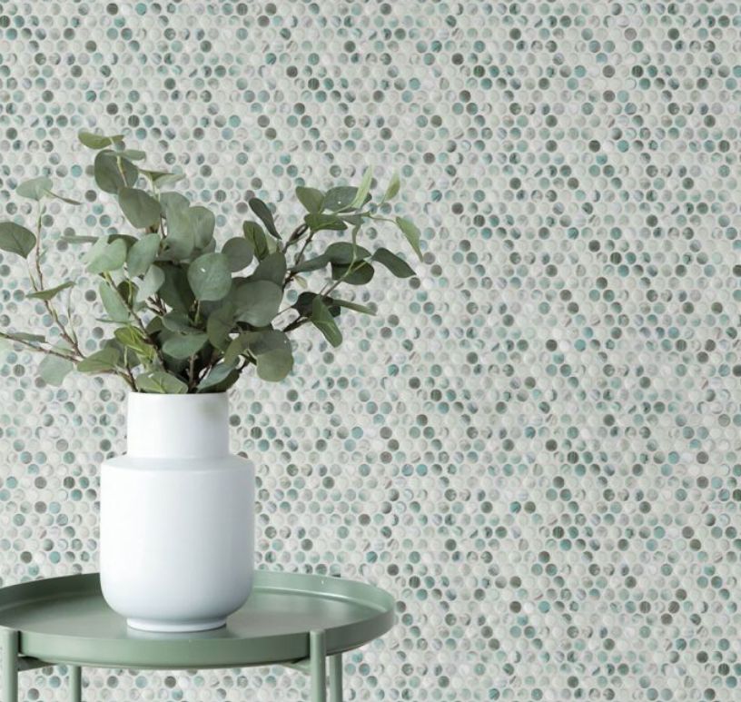 Vase with eucalyptus on a mint table, in front of a wall with round, speckled tiles.