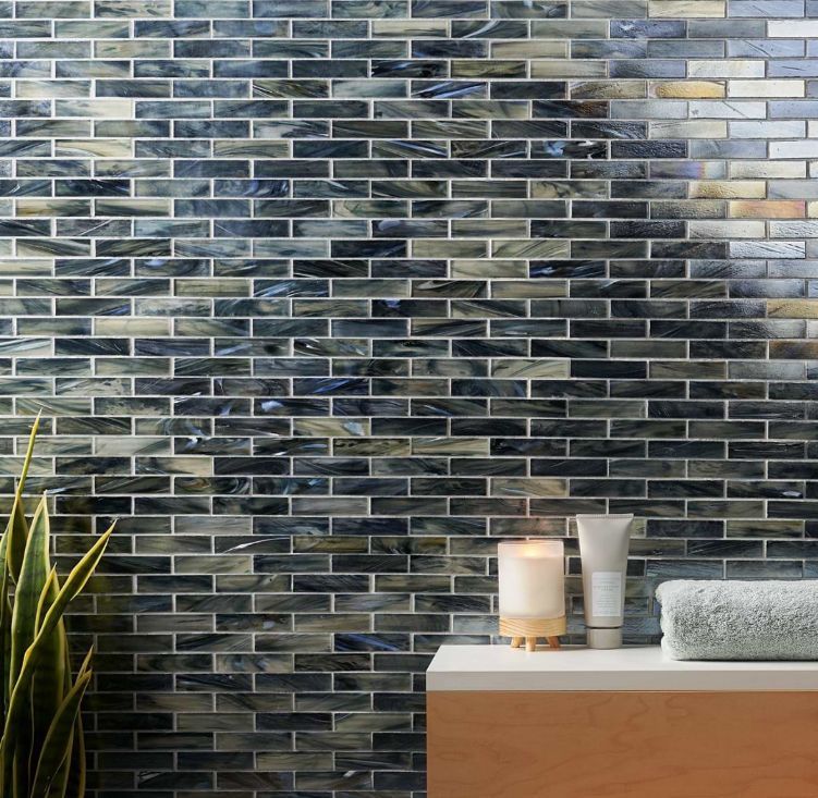 Dark blue, gray, and cream mosaic tile wall. A white counter with a candle, lotion, and towel. A plant.