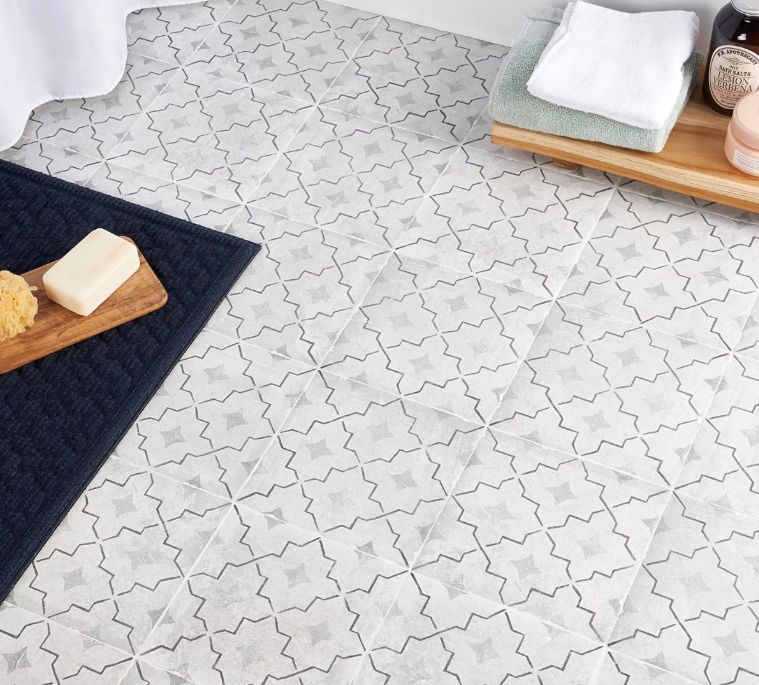 Bathroom floor with patterned tiles. Dark blue bath mat with soap and sponge. Towels and toiletries on a wooden tray.