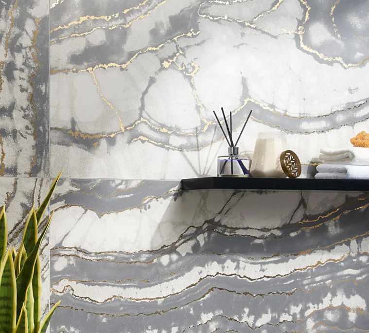 Bathroom wall with marble-like gray and white tile, gold veins, and a black shelf with accessories.