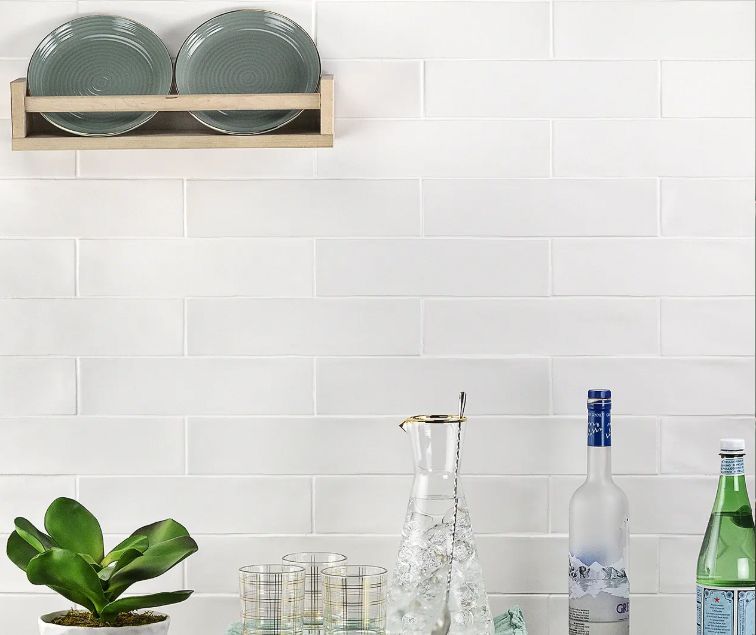 White tiled kitchen with dish rack, plant, and bottles.