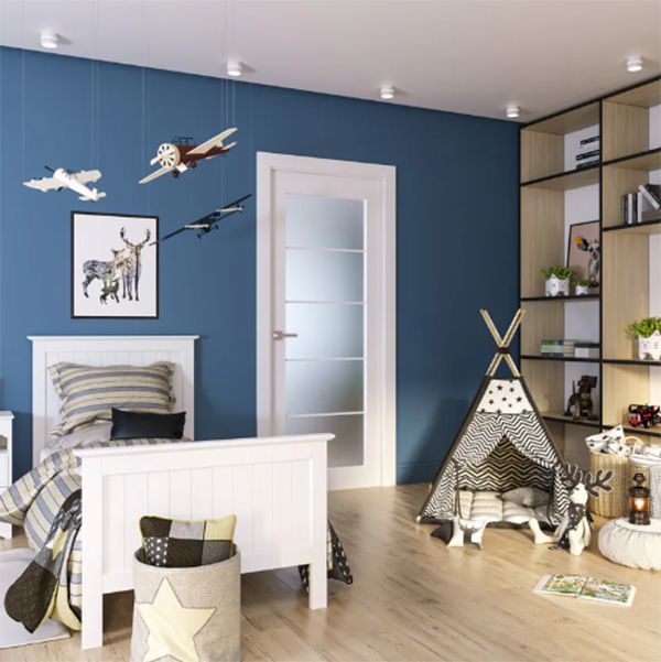 Child's bedroom with white bed, teepee, bookshelf, and airplanes hanging from the ceiling. Blue wall and light wooden floor.
