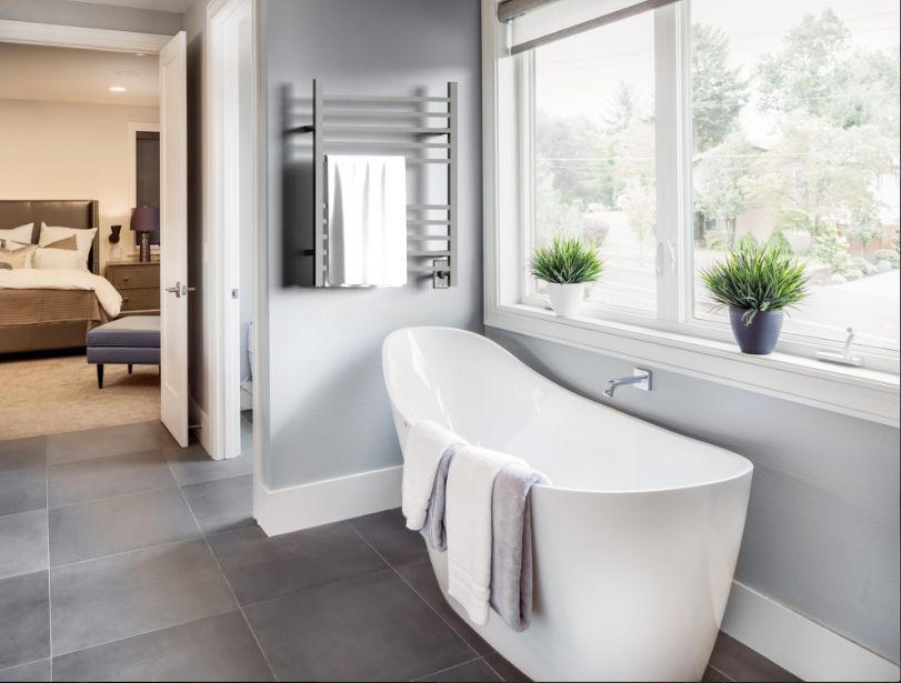 Modern bathroom with a white tub, towels, and a heated towel rack near a window.