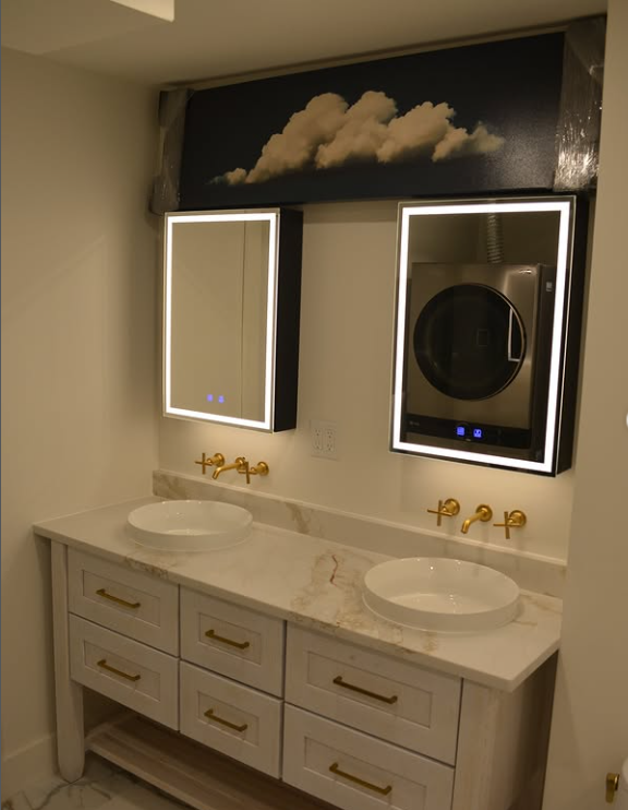 Bathroom vanity with two sinks, two mirrors, and a washing machine behind the right mirror. White, gold, and marble accents.
