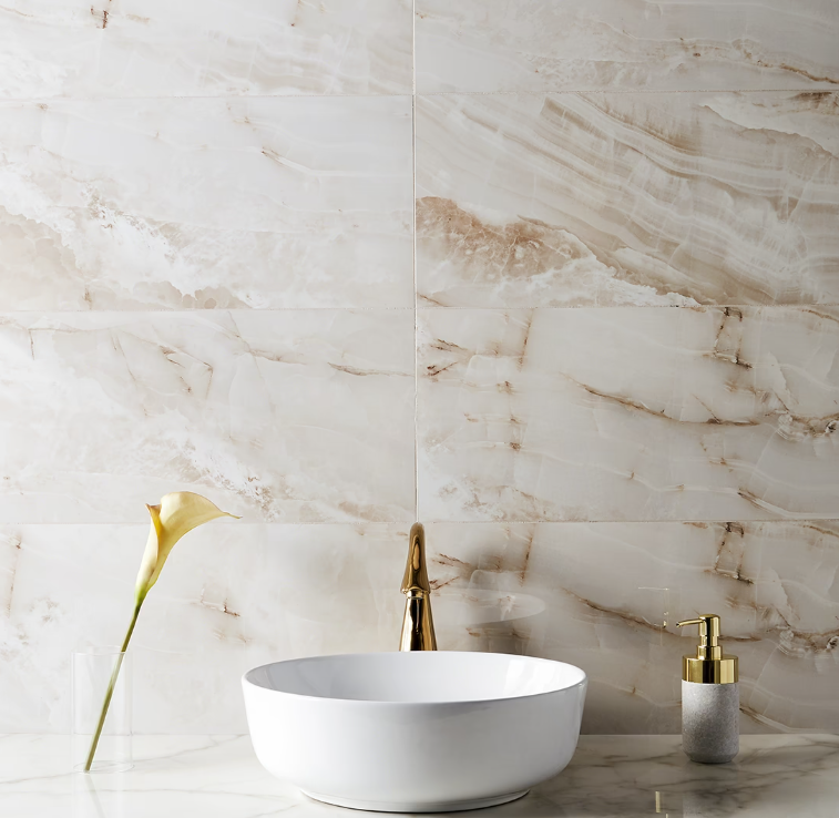 White vessel sink and gold faucet against marble tile wall.
