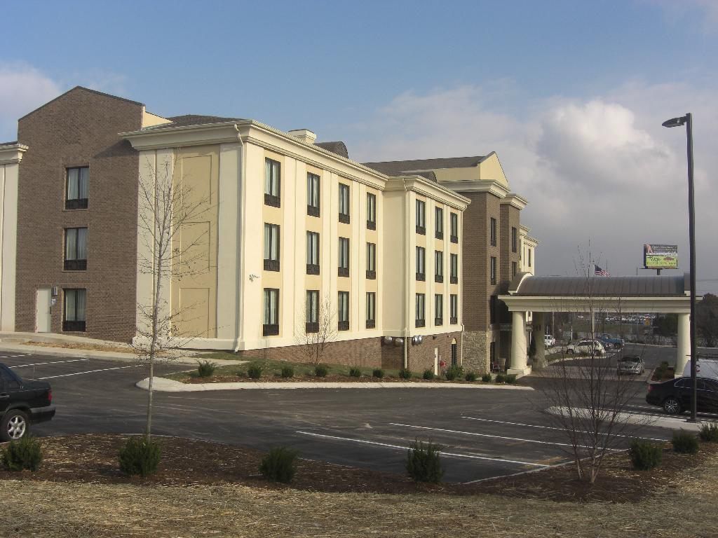 Hotel with beige facade, brown brick accents, parking lot, and covered entrance. Sunny day.