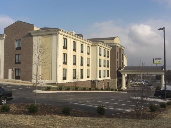 Hotel with beige facade, brown brick accents, parking lot, and covered entrance. Sunny day.