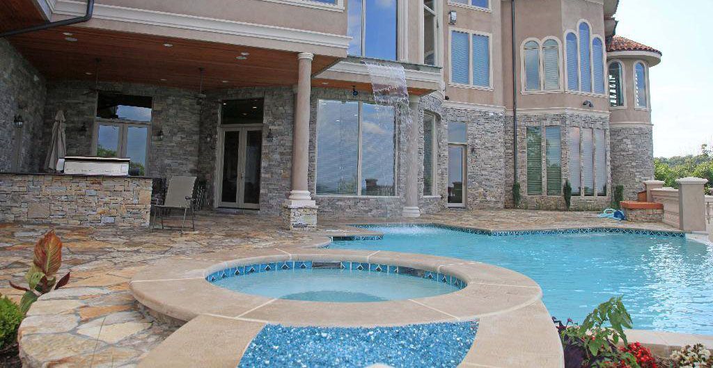 Luxury home exterior with pool and hot tub; stone and stucco facade.
