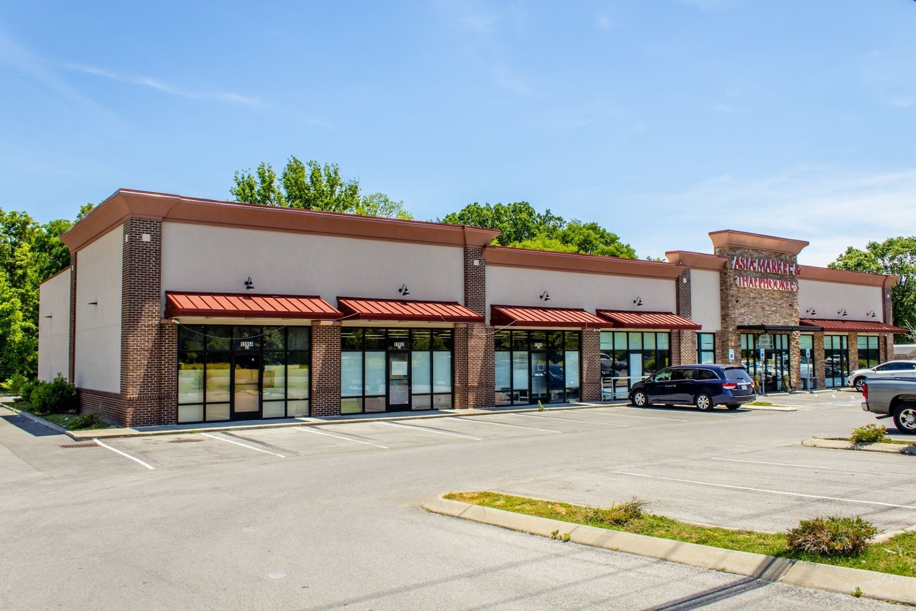 A single-story commercial building with multiple storefronts and a parking lot on a sunny day.