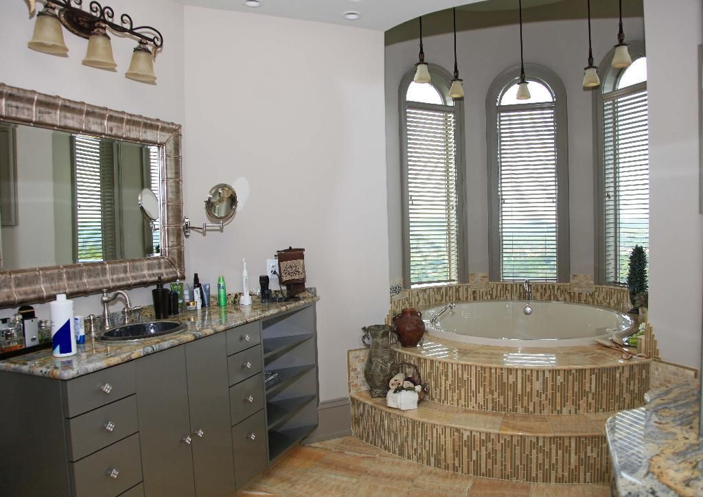 Bathroom with granite countertop, large mirror, and a tub with decorative stone steps.