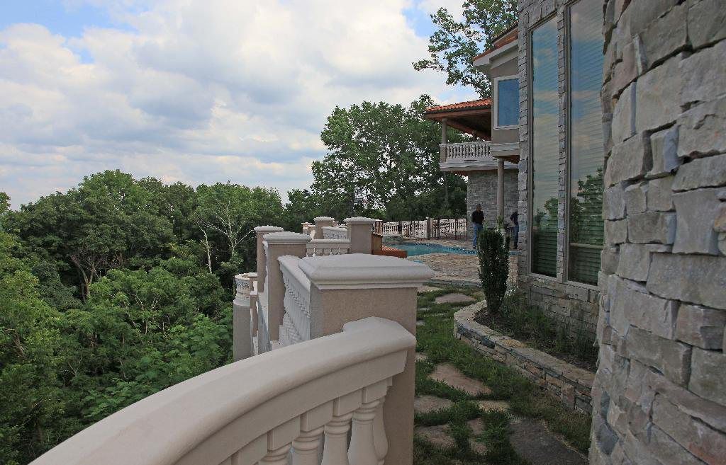 Stone mansion with a balcony overlooking a wooded area and a pool.