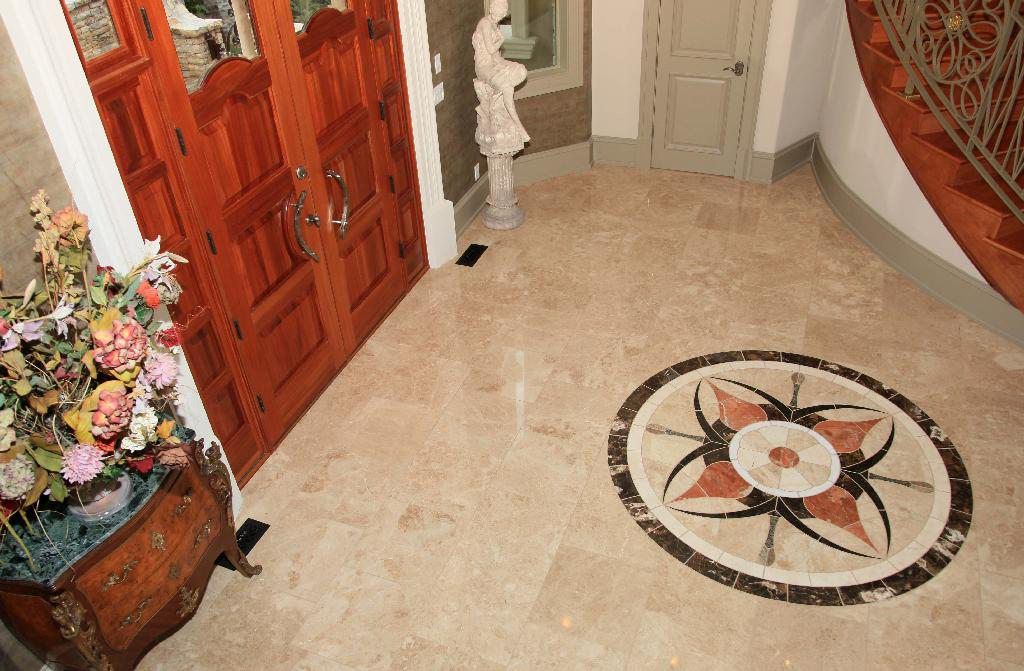 Ornate wooden doors open to a beige marble floored entryway, featuring a circular tile design.
