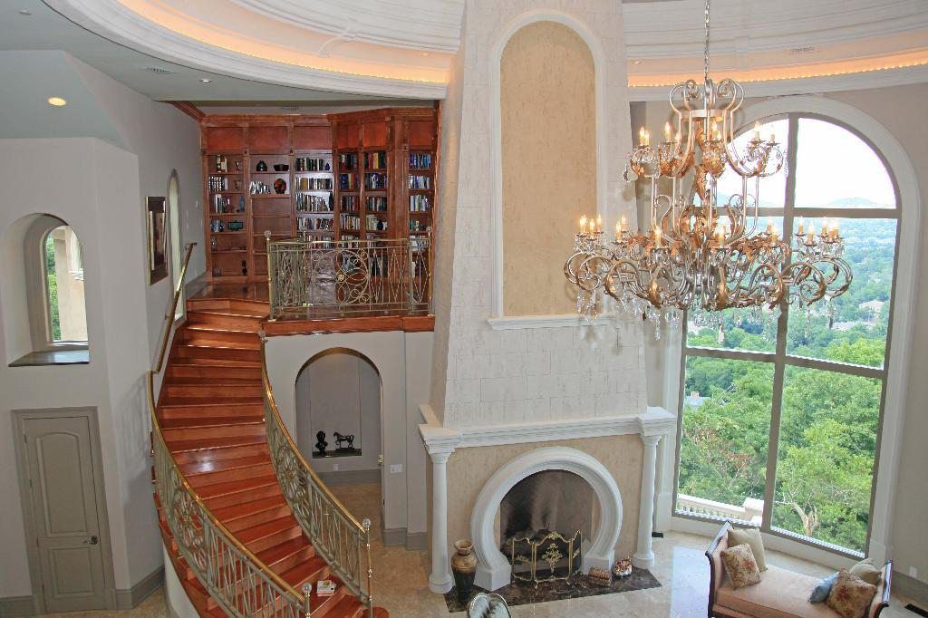 Grand foyer with a staircase, fireplace, and chandelier; overlooking a forest view.